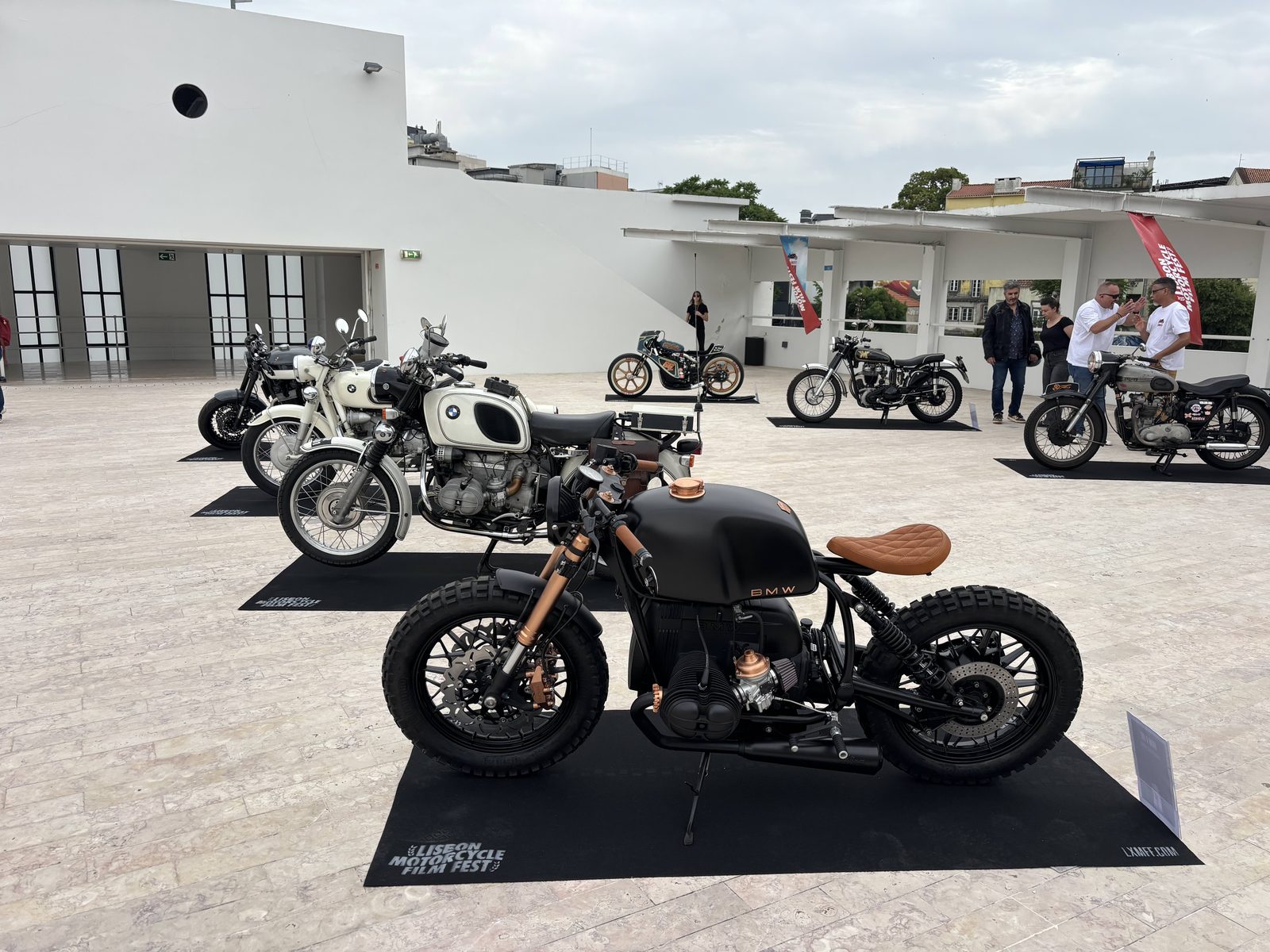 Кастом и классические мотоциклы BMW на выставке Lisbon Motorcycle Film Fest 2026, на переднем плане матовый чёрный BMW boxer cafe racer.